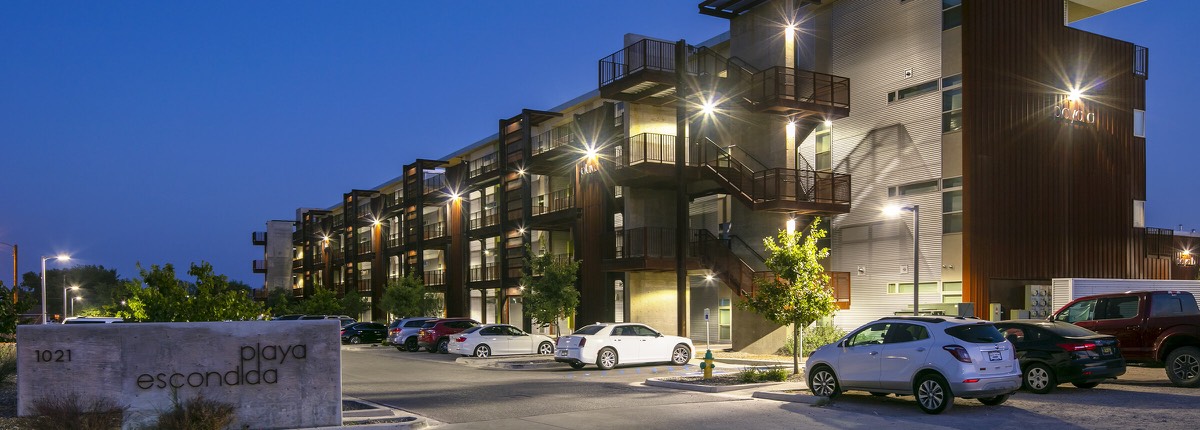 Evening view of the lit Playa Escondida apartment community along Yeso Drive in Hobbs with cars parked out front