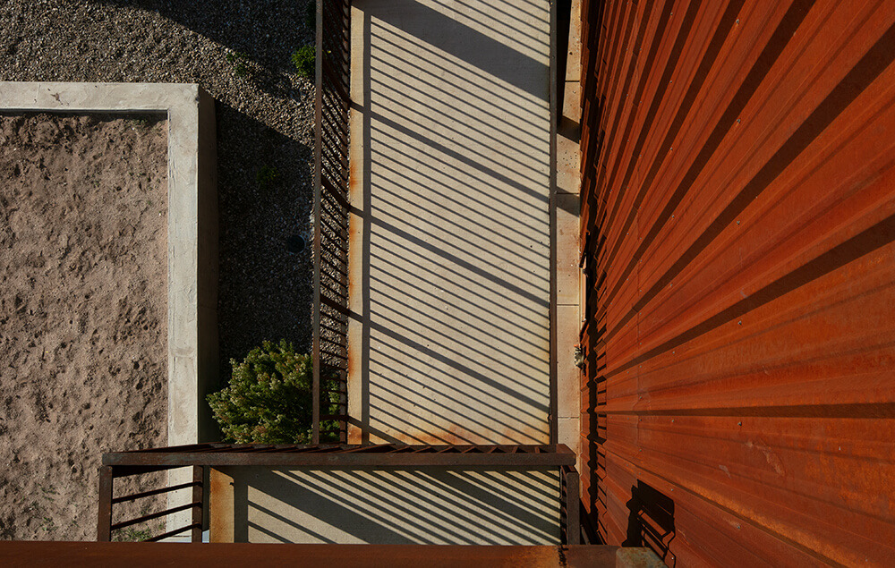 Overhead view of corrugated steel siding, balcony shadows, and xeriscape ground at Playa Escondida