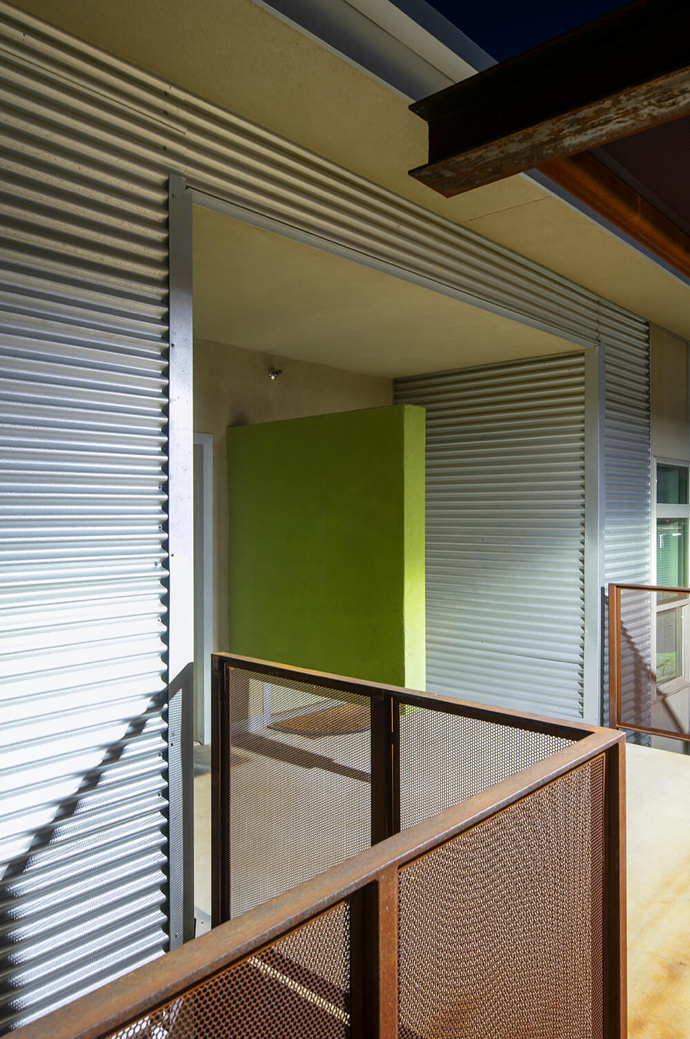 Upper-floor breezeway at Playa Escondida in Hobbs at dusk, with a bright green accent wall and corrugated-steel siding