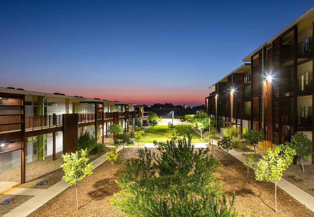 Green central courtyard with lawns and young trees between apartment buildings at Playa Escondida at sunset